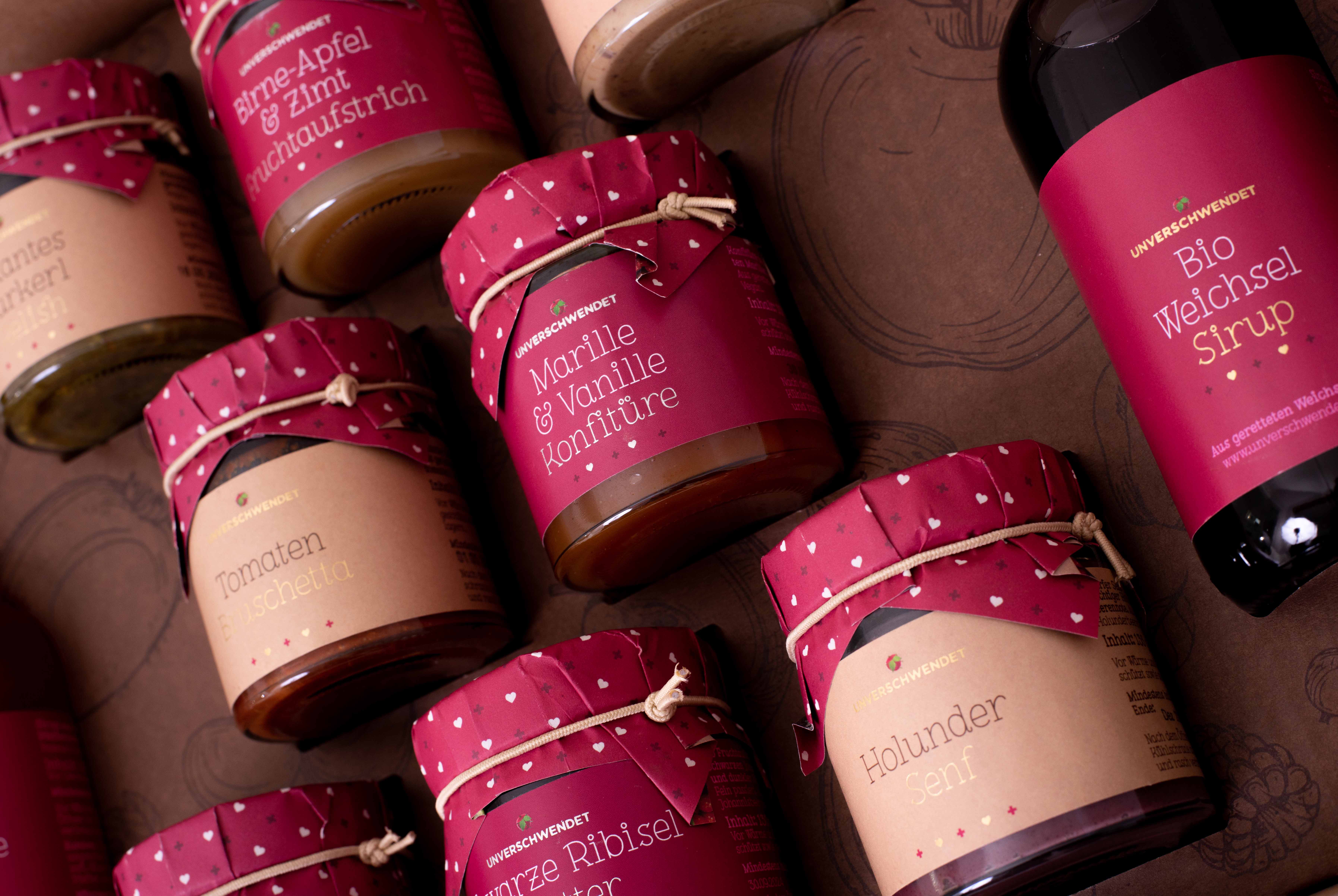 Nahaufnahme von geöffneter Geschenkbox mit Aufstrich-Gläschen und Sirup als Inhalt (von oben) Nahaufnahme von geöffneter Geschenkbox mit Aufstrich-Gläschen und Sirup als Inhalt
