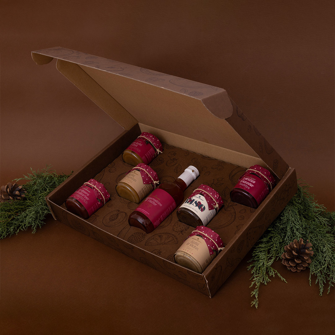 Geöffneter Geschenkkarton mit Aufstrich-Gläschen und Sirup (von der Seite) Geöffneter Geschenkkarton mit Aufstrich-Gläschen und Sirup